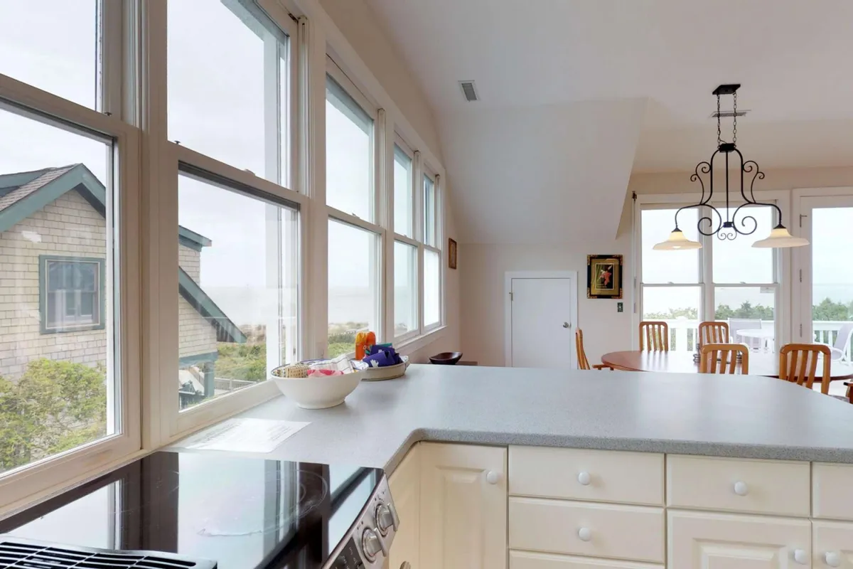 An inviting open-concept space featuring a large kitchen counter, a stylish dining table, and soaring windows that flood the area with natural light and offer panoramic ocean views. A modern chandelier adds warmth and sophistication, while the expansive layout encourages gathering and entertaining.
