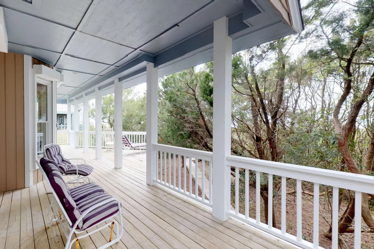 A tranquil porch with a wooden railing and striped chairs nestled among leafy trees, offering a shaded, private outdoor retreat. The space feels cool and inviting, ideal for unwinding after outdoor adventures.