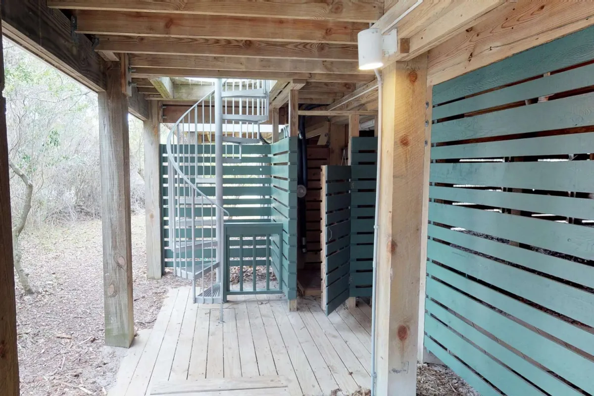 A light-filled interior space with an open plan design, featuring a spiral staircase and wooden slats. This area hints at the entryway and the connection between levels, suggesting a welcoming transition into the home.