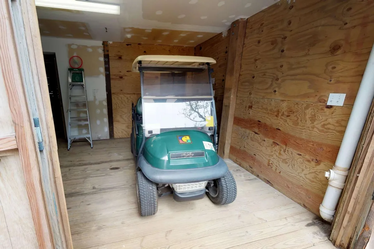 The image features a practical interior garage space with wooden walls and flooring, centered around a golf cart. The space is clean and uncluttered, showcasing storage solutions and highlighting readiness for island exploration.