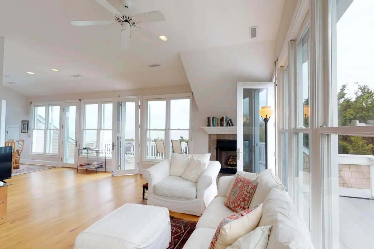 A comfortable living room with a white sofa, stylish coffee table, fireplace, and expansive windows offering impressive sunrise views. The setup suggests both relaxation and social interaction, emphasizing natural light and the indoor-outdoor connection.