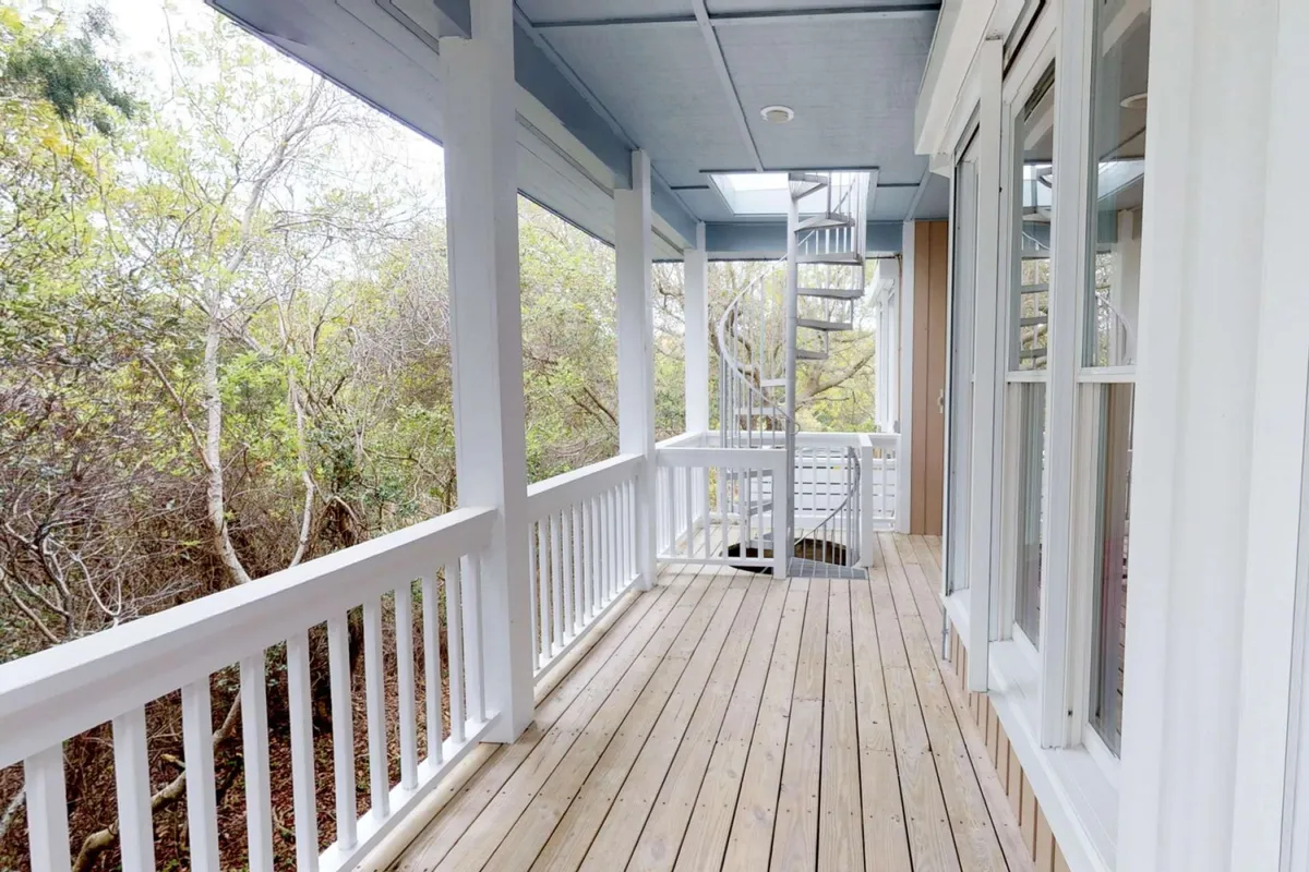 A striking exterior shot of the wooden deck with a spiral staircase, surrounded by greenery. The deck invites morning coffees or evening stargazing, while the distinctive staircase serves as a dramatic architectural feature connecting interior and exterior spaces.
