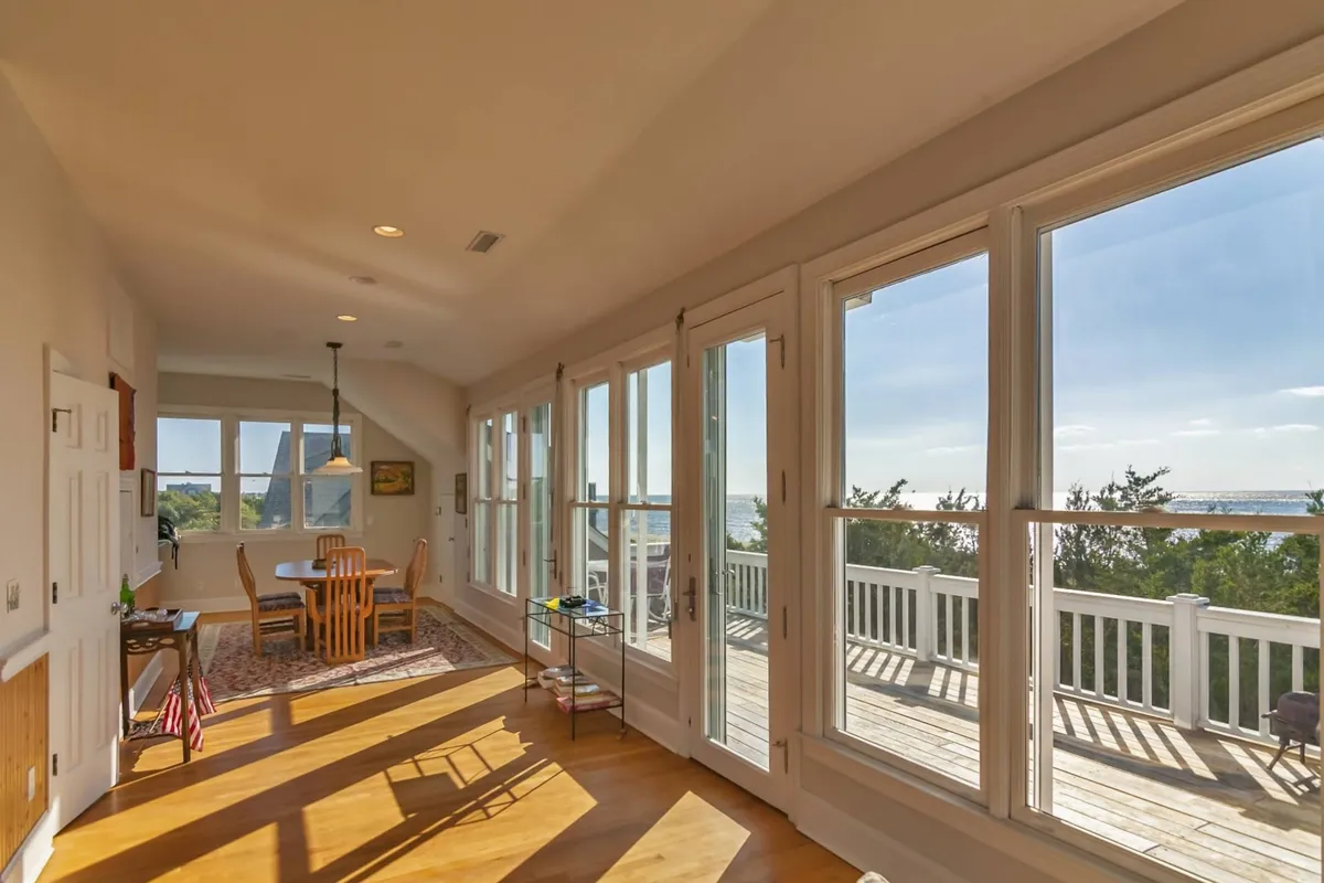 A relaxed and welcoming interior featuring a dining table with wooden flooring and expansive windows framing a scenic view. The space is ideal for family meals, morning coffee, or quiet moments by the window.