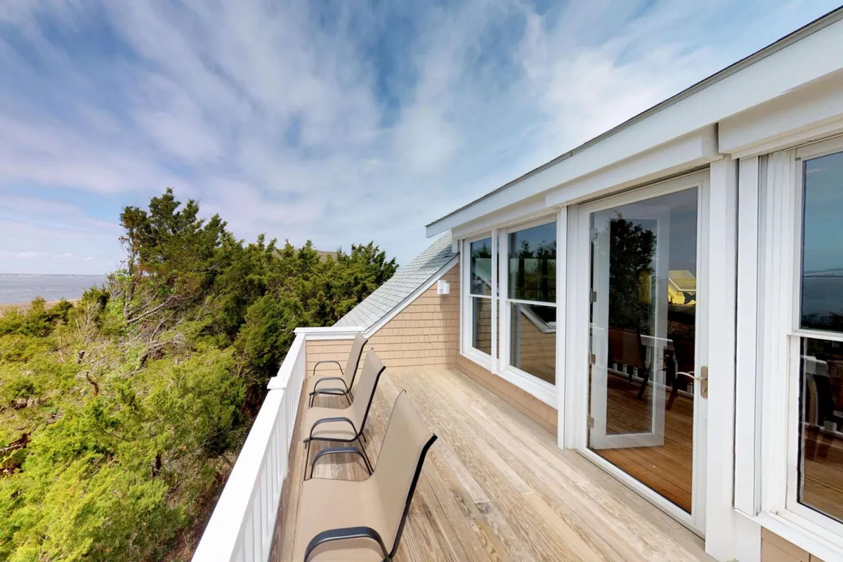 The image showcases a peaceful deck framed by natural greenery, furnished with inviting deck chairs that face out through glass doors toward open skies. The scene suggests a tranquil spot perfect for relaxing, socializing, or enjoying the breathtaking sunrise and evening stars.
